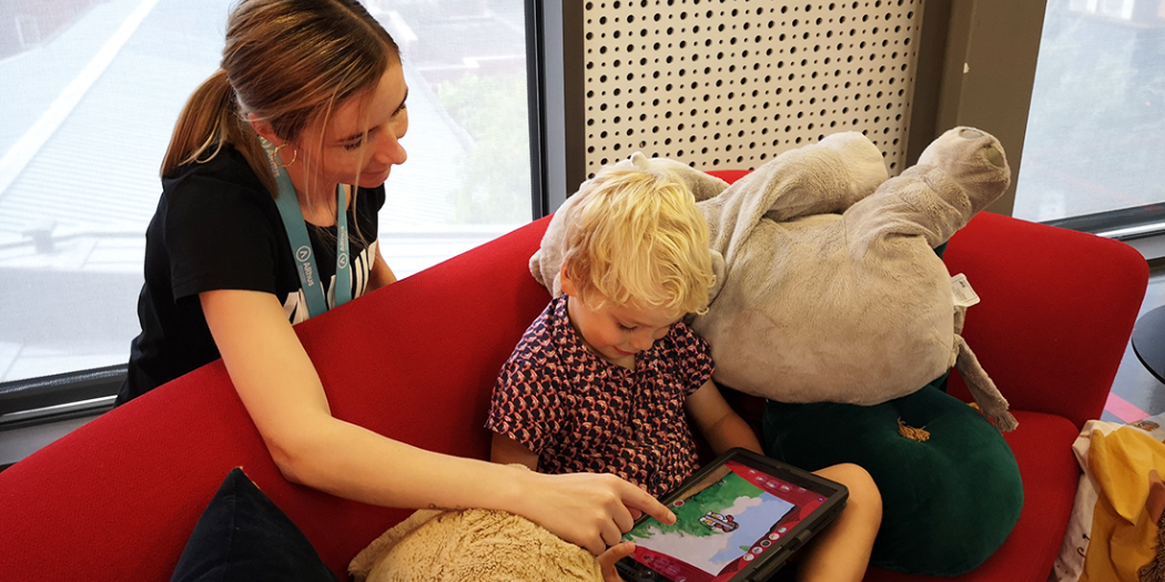 Kindje op bank met tablet en vrouw achter hem.