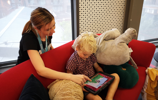 Kindje op bank met tablet en vrouw achter hem.